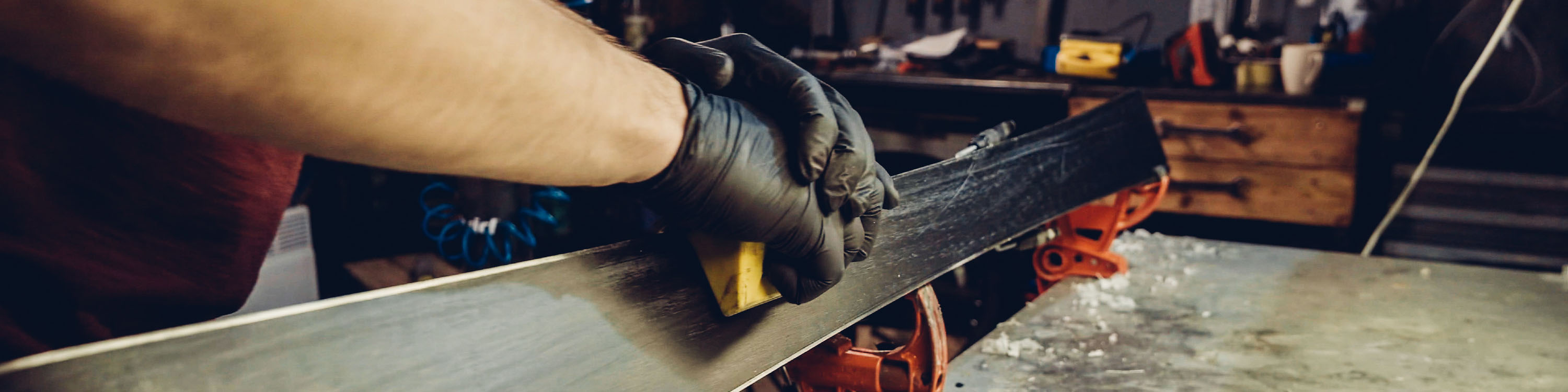 Image of a ski tech tuning a pair of skis on a bench.